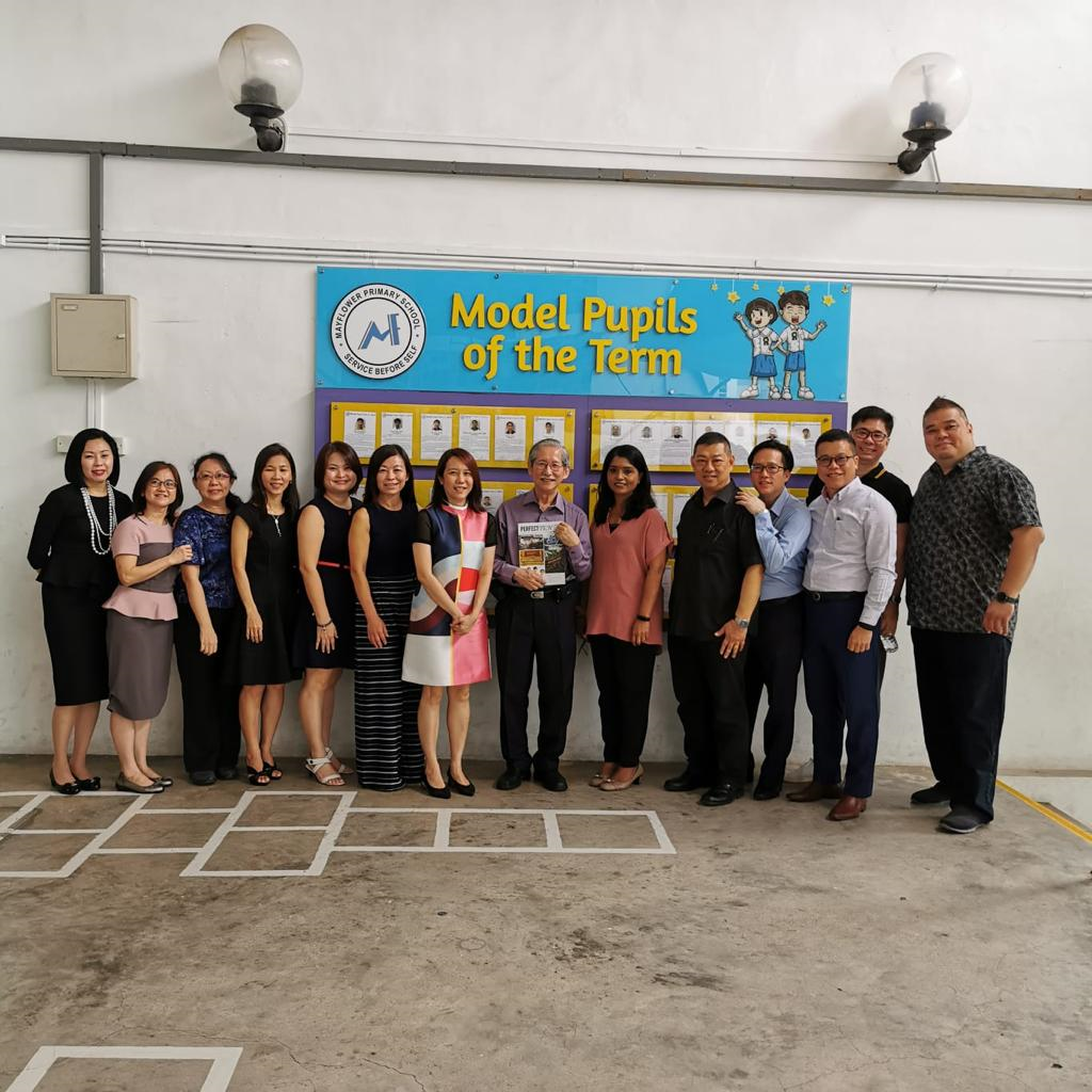 Group of adults posing in front of a blue "Model Pupils of the Term" banner at Mayflower Primary School.